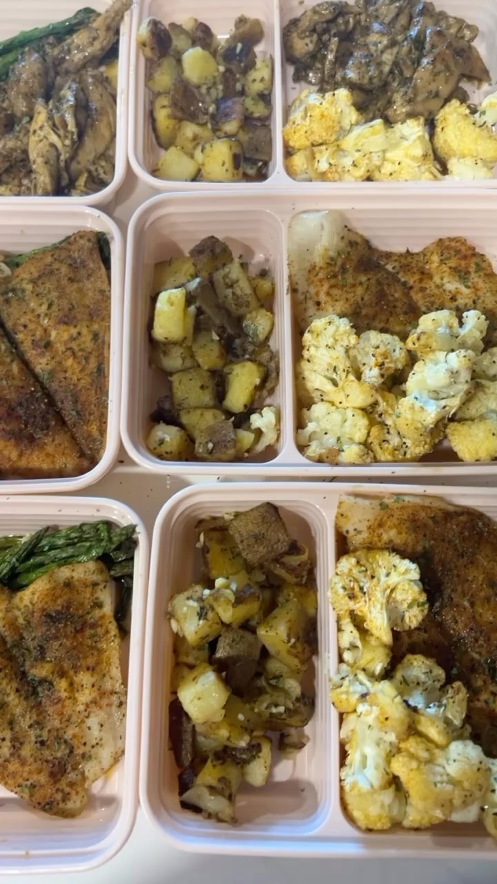 Pink meal prep containers filled with seasoned fish, chicken, roasted potatoes, cauliflower, and asparagus arranged in neat rows on a countertop.